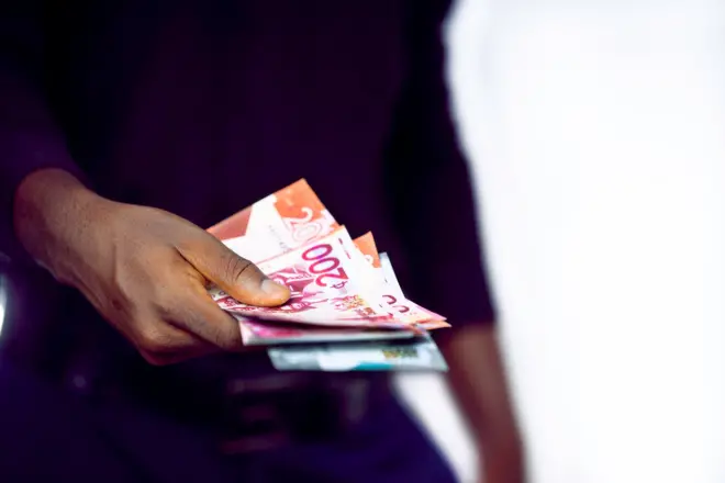Homme noir en chemise noire à manches longues tenant des billets de cedi ghanéen.